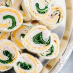 Sliced pinwheel sandwiches with turkey, cheddar, and spinach on a platter