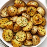 Golden roasted baby potatoes in white ceramic bowl with herbs
