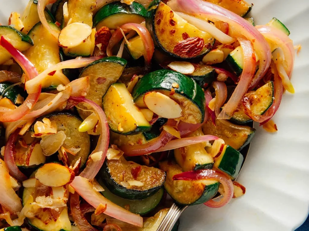 Sautéed zucchini with red onion and almonds in white bowl