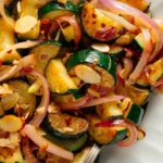 Sautéed zucchini with red onion and almonds in white bowl