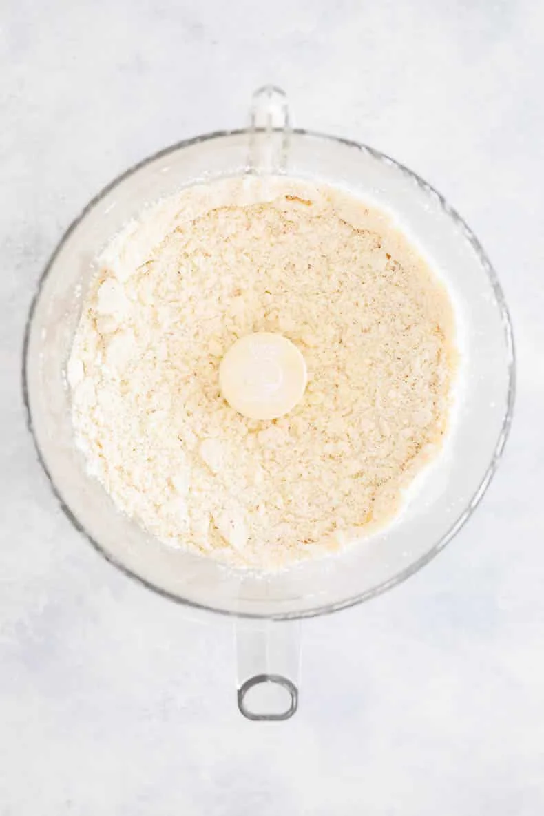 Food processor bowl holding dry almond flour pastry ingredients