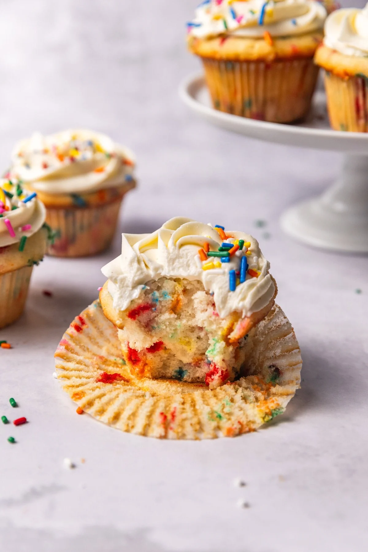 Frosted funfetti cupcakes with sprinkles on a light countertop