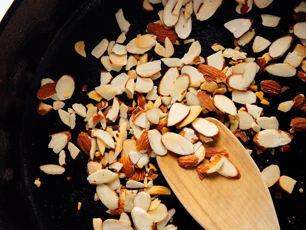 Sliced almonds toasting in a cast iron skillet