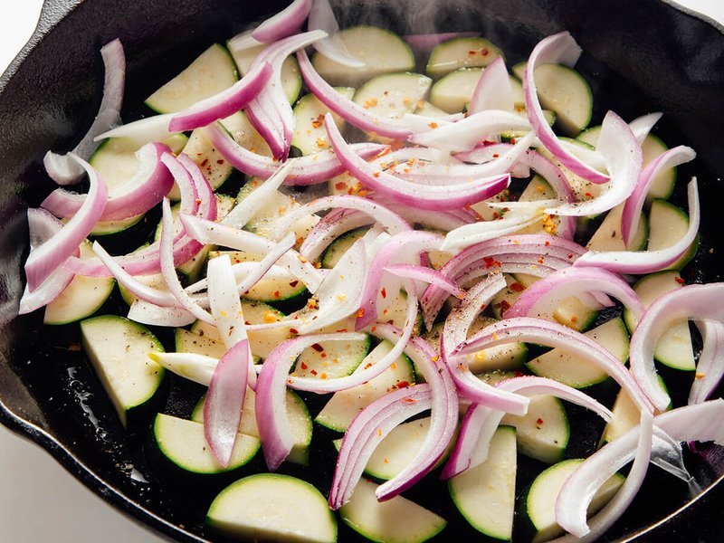 Zucchini and red onion cooking in a skillet