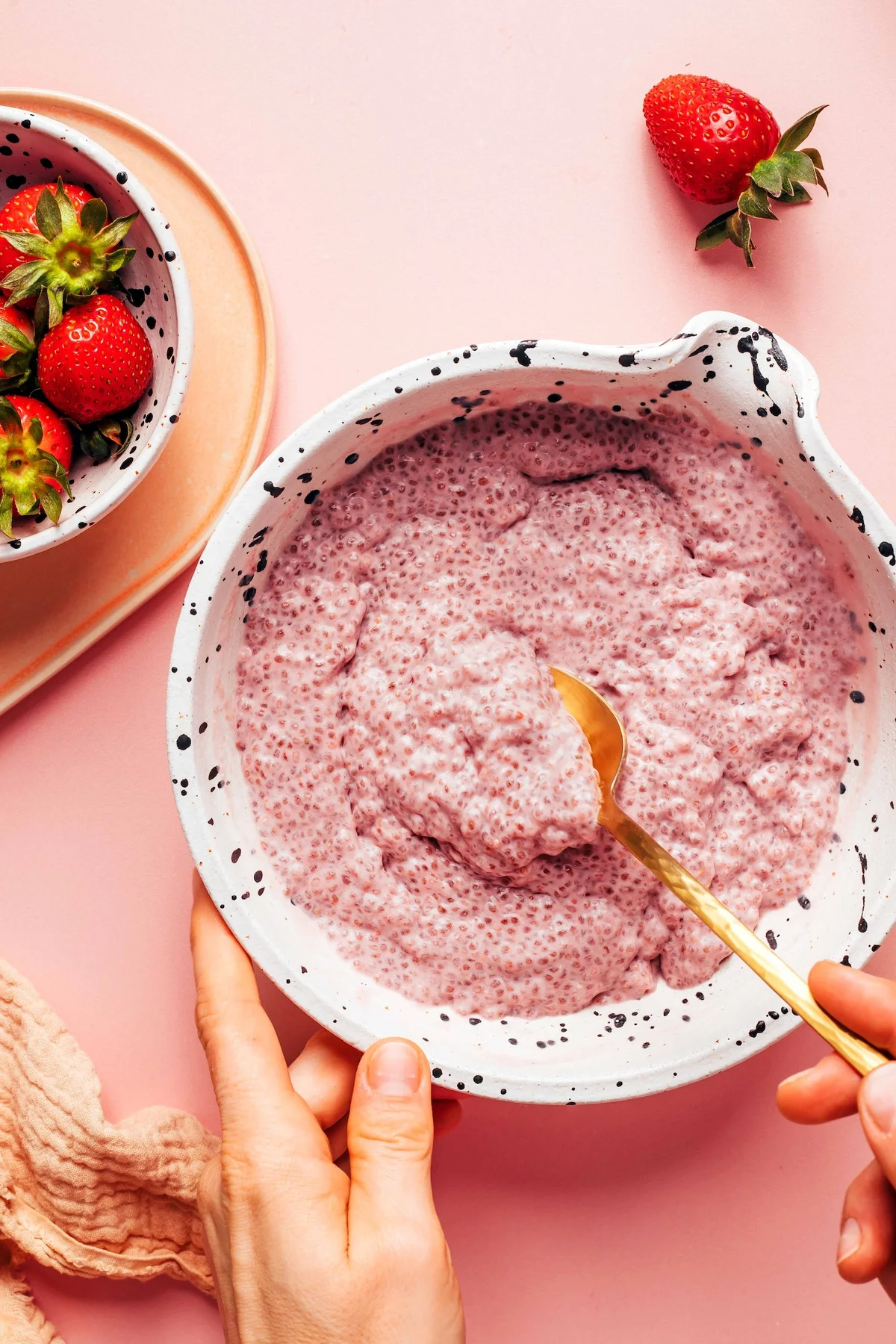 Hands lifting a spoonful of strawberry chia pudding from a bowl