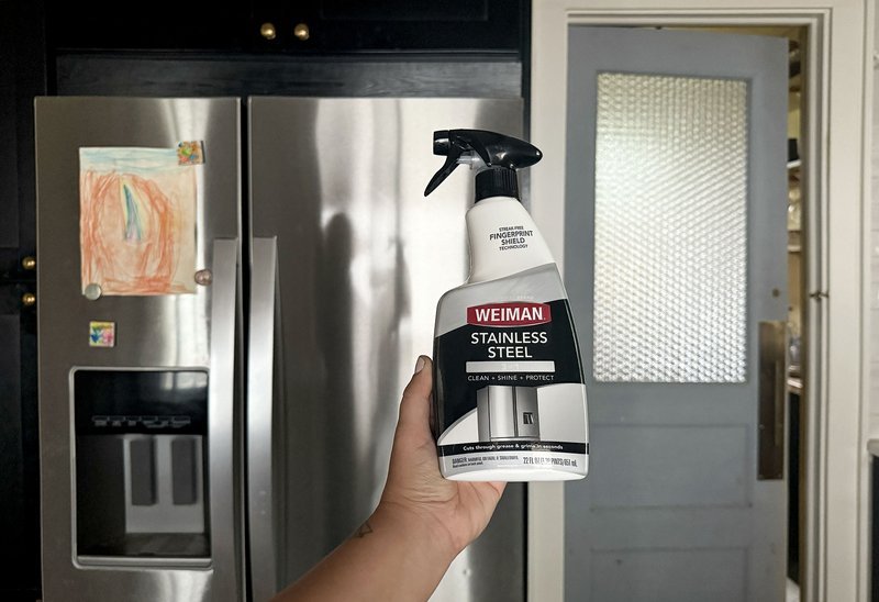 Hand holding stainless steel cleaner in front of fridge