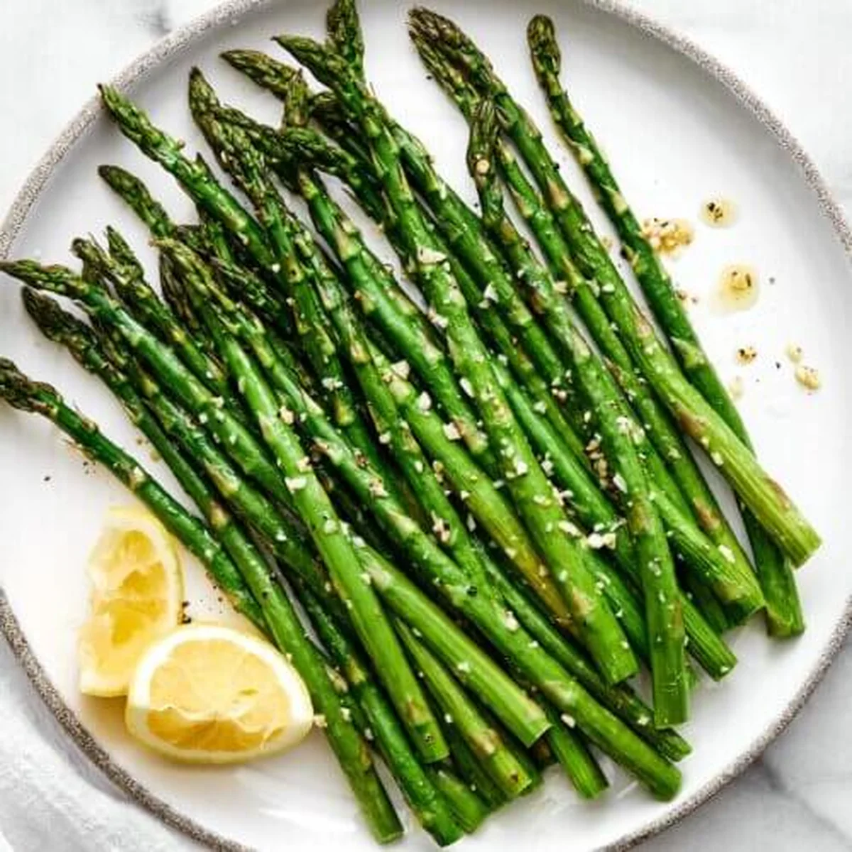 Roasted asparagus spears on white plate with lemon wedges