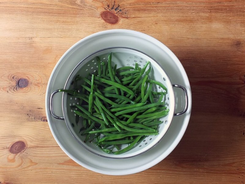 Drained green beans cooling in a bowl of cold water
