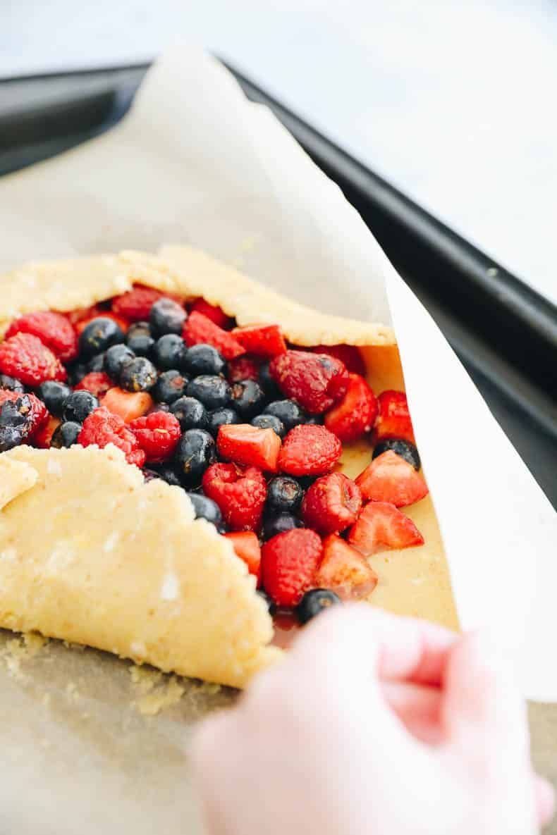 Hands folding the galette crust edges over the berries