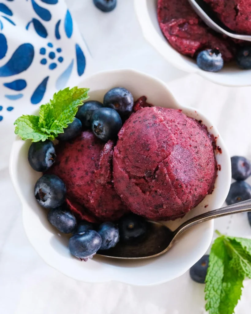 Bowl of deep purple three-ingredient blueberry sorbet with fresh blueberries
