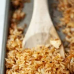 Golden crispy rice on a baking sheet with wooden spoon