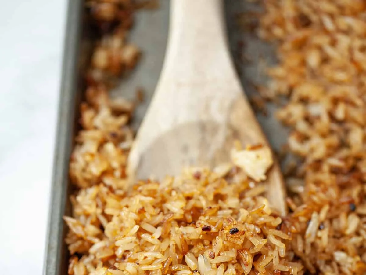 Golden crispy rice on a baking sheet with wooden spoon