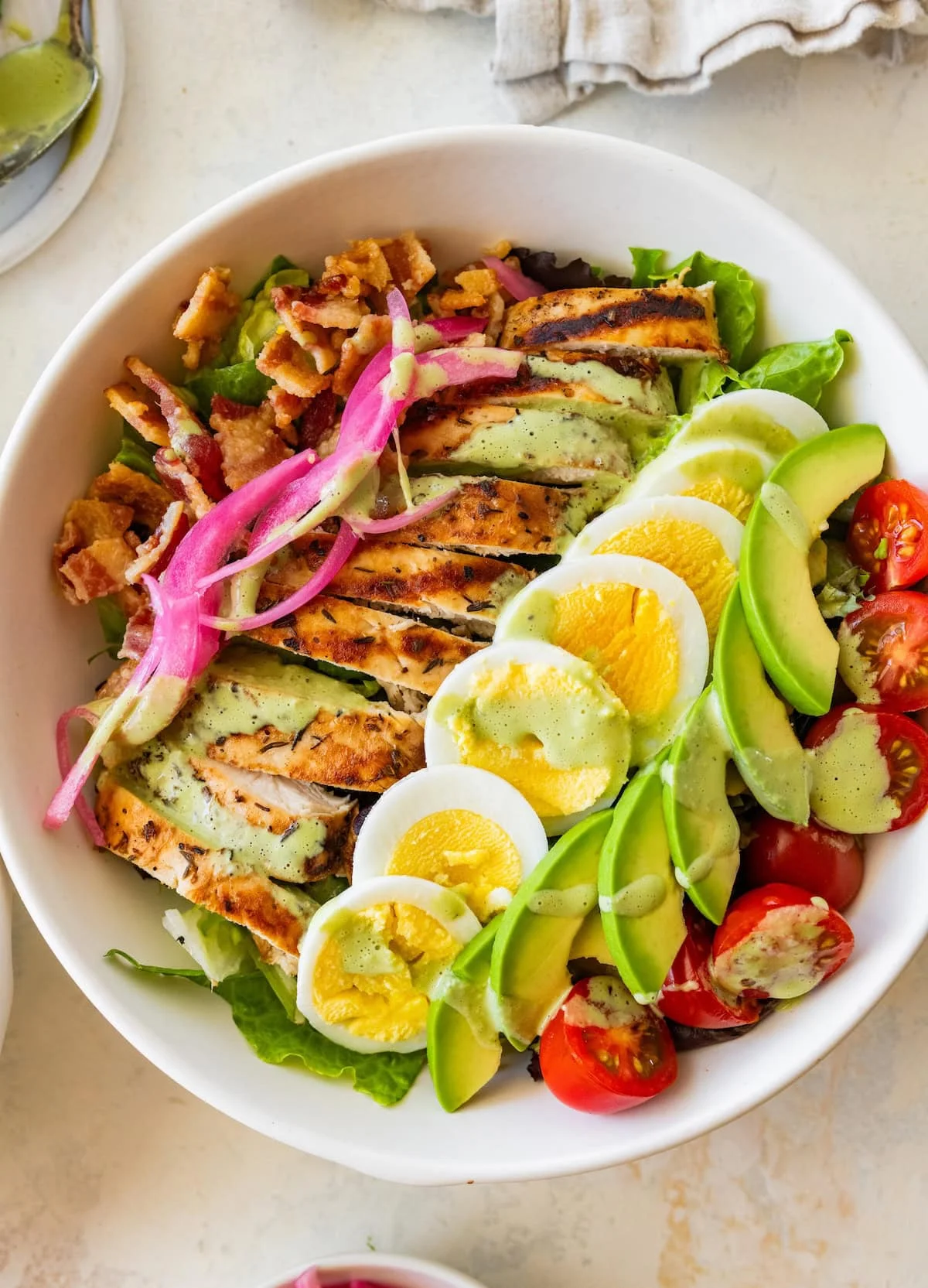 Overhead view of loaded green goddess cobb salad bowls with chicken, avocado and green dressing