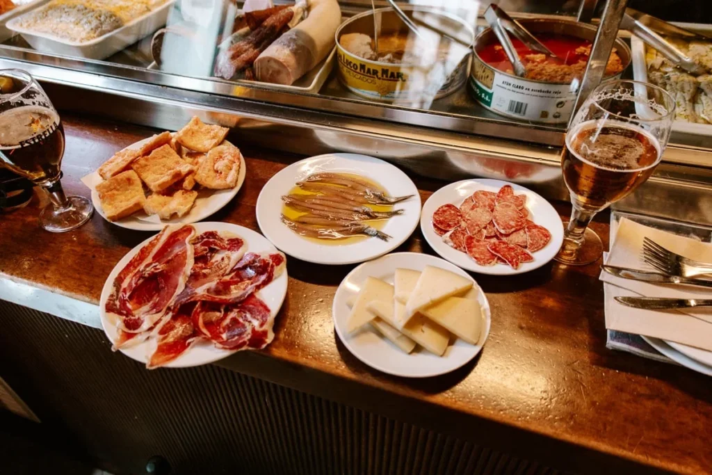 Small tapas plates of jamón, anchovies and cheese with beer on a bar counter