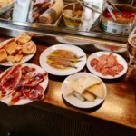 Small tapas plates of jamón, anchovies and cheese with beer on a bar counter