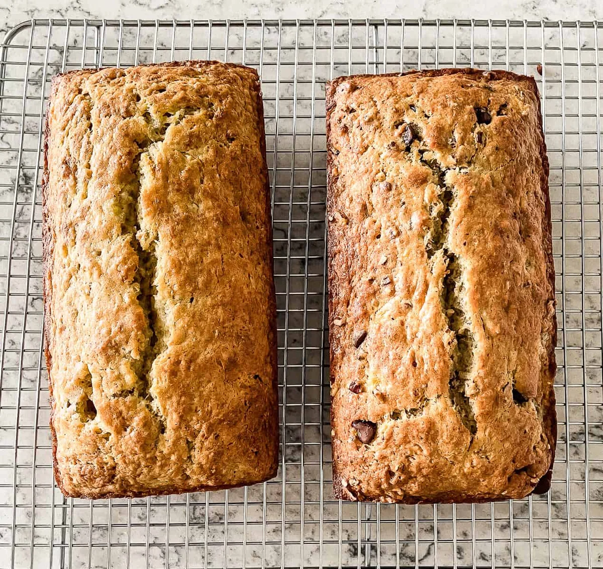Two golden loaves of sourdough banana bread cooling on a wire rack