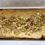 Sliced pistachio cake loaf topped with chopped pistachios