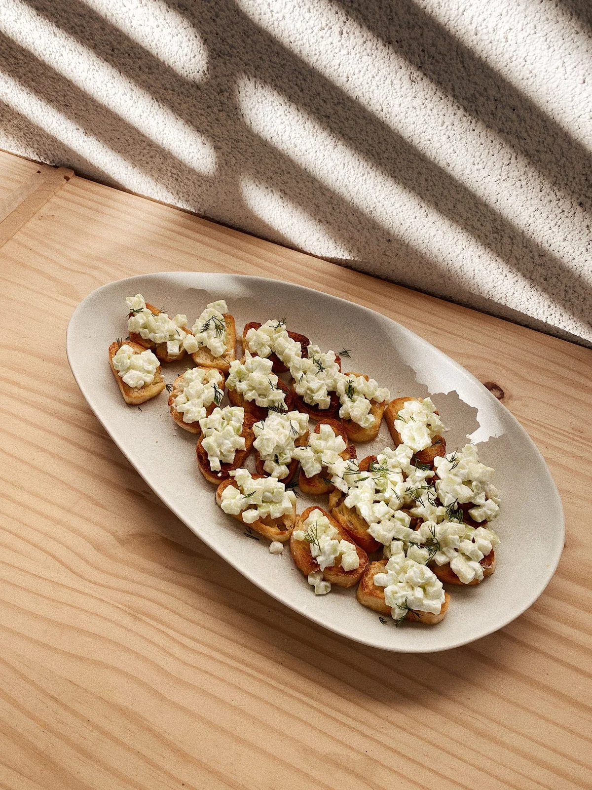 Crostini topped with creamy cucumber yogurt dip and fresh dill on a ceramic plate