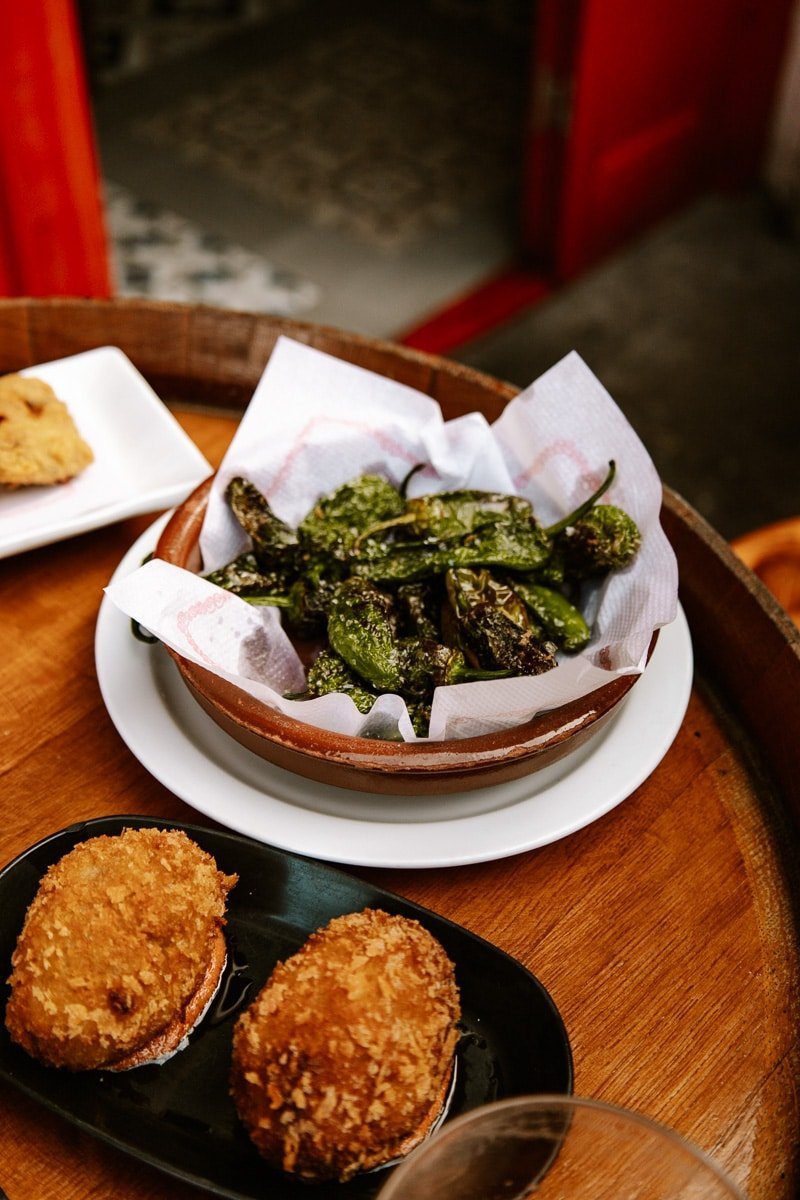 Charred padrón peppers and golden croquettes on a wooden tapas tray