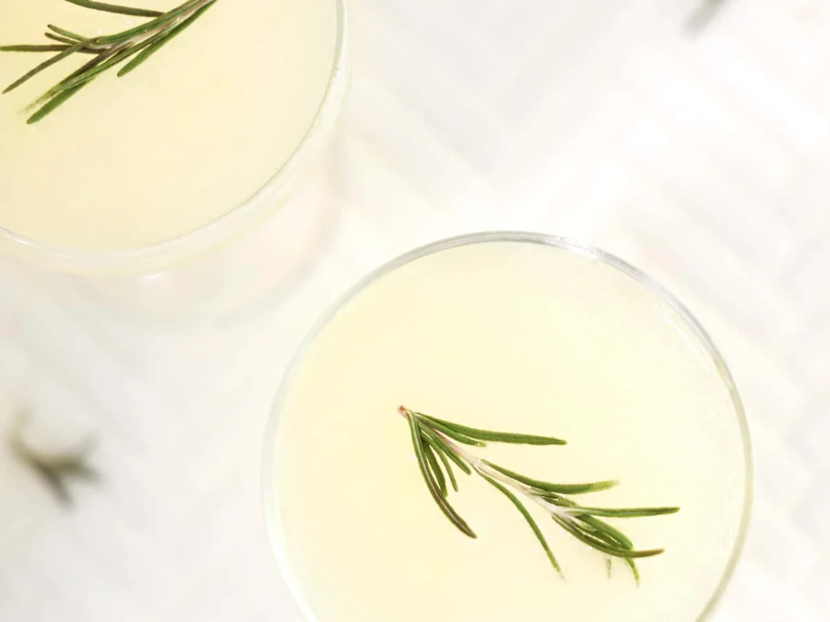 Two glasses of gimlet garnished with rosemary on a white marble surface