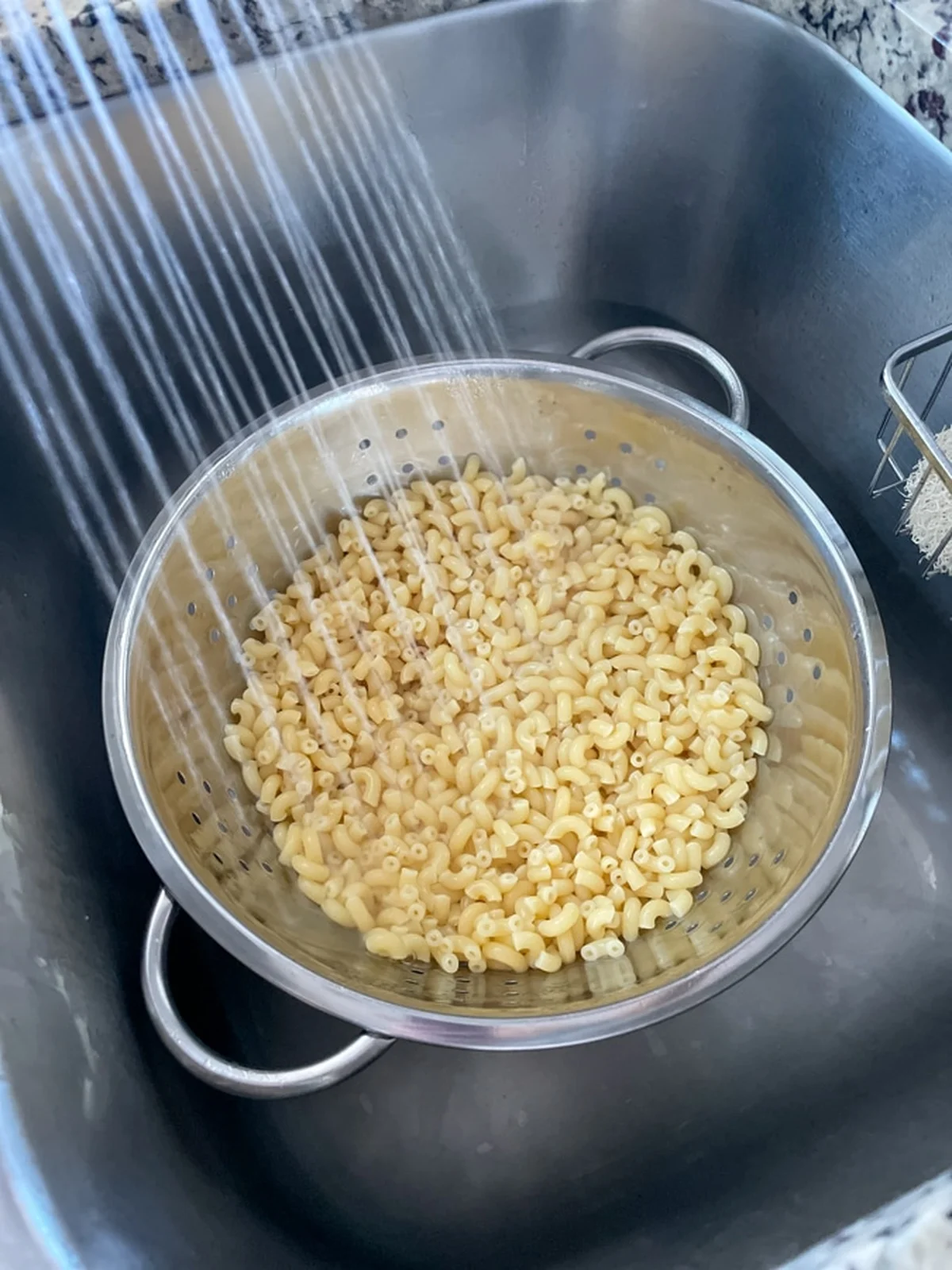 Cooked elbow macaroni rinsed in a colander under running water