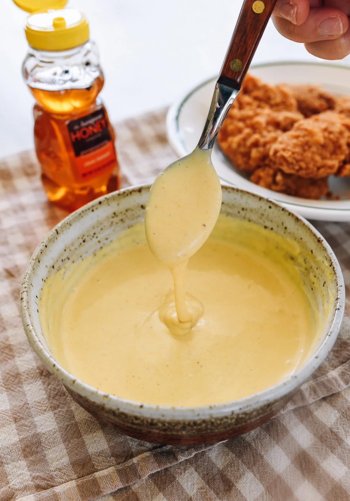 Bowl of thick honey mustard sauce beside fried chicken and a honey bottle