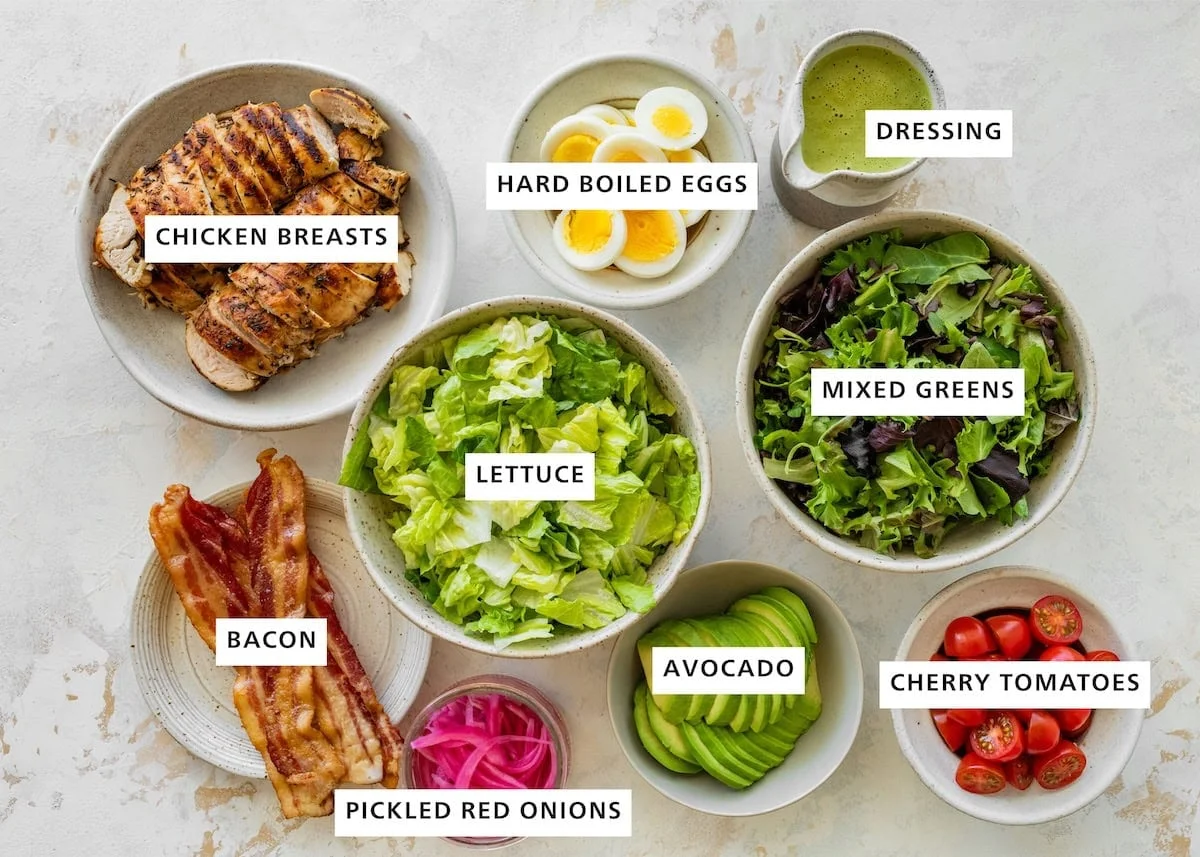 Flat-lay of salad ingredients in labeled bowls on a marble surface