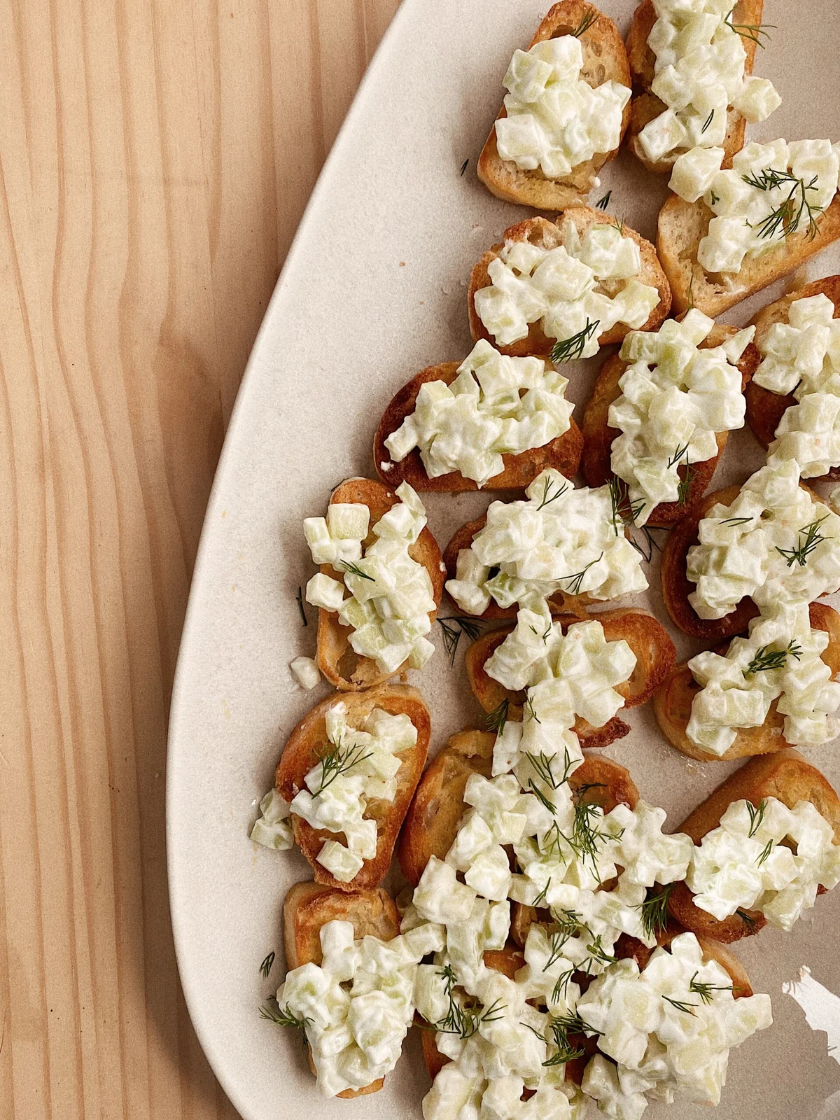 Top-down view of cucumber and yogurt crostini on a rustic wooden board