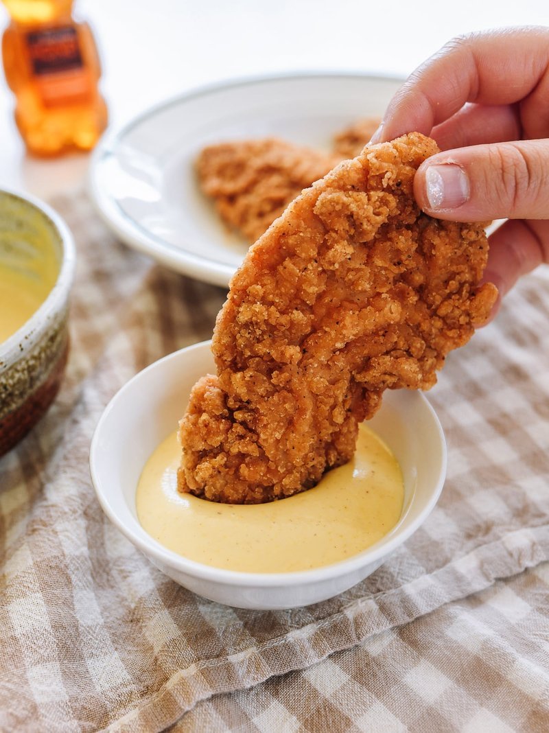 Hand dipping a golden fried chicken cutlet into honey mustard sauce