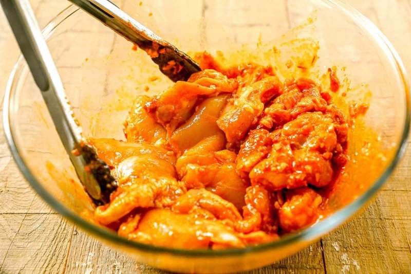 Raw chicken thighs coated in harissa marinade in a glass bowl