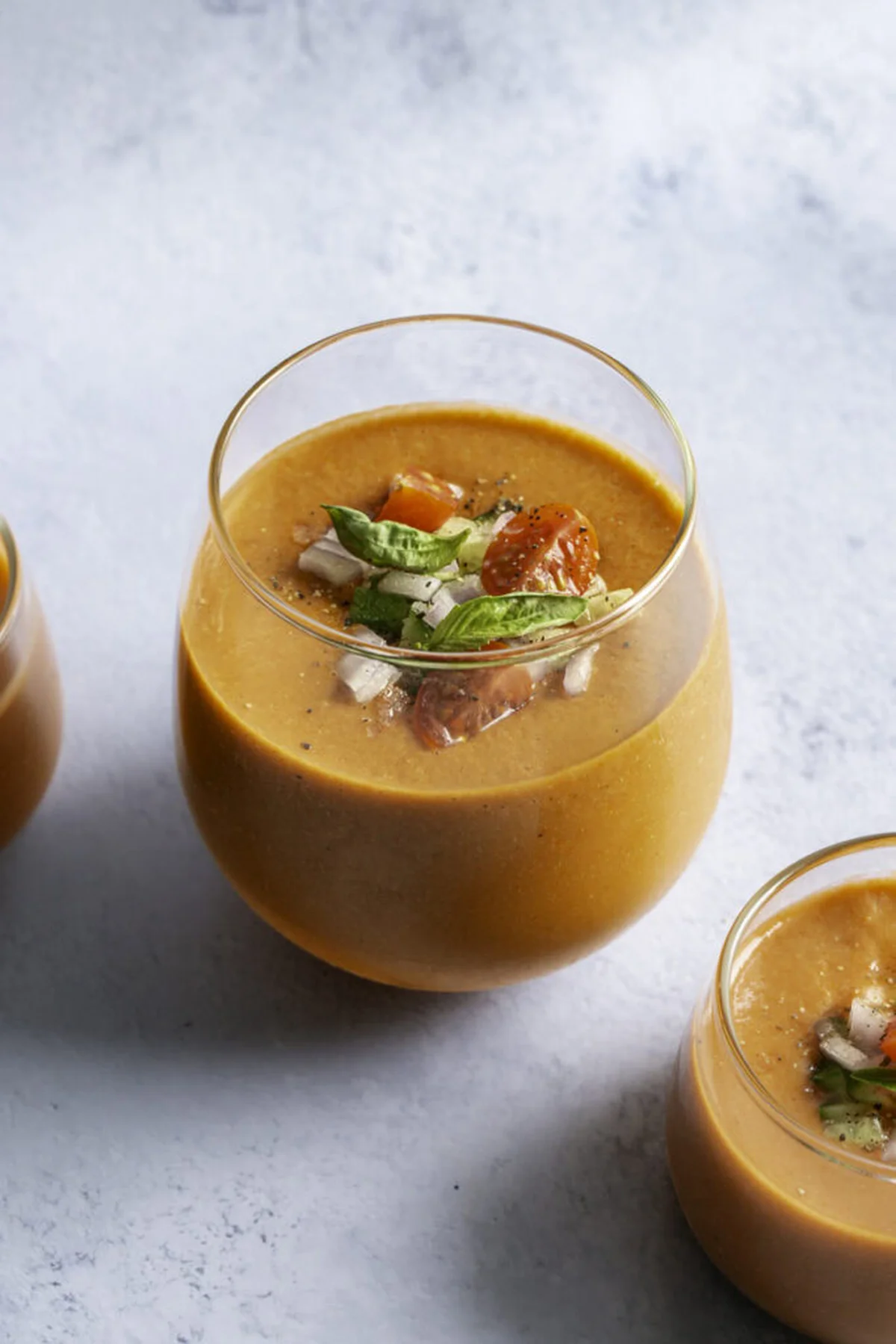 Glasses of chilled cherry tomato gazpacho with fresh herb garnish