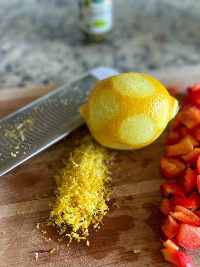Zested lemon with zester and diced red bell pepper on cutting board