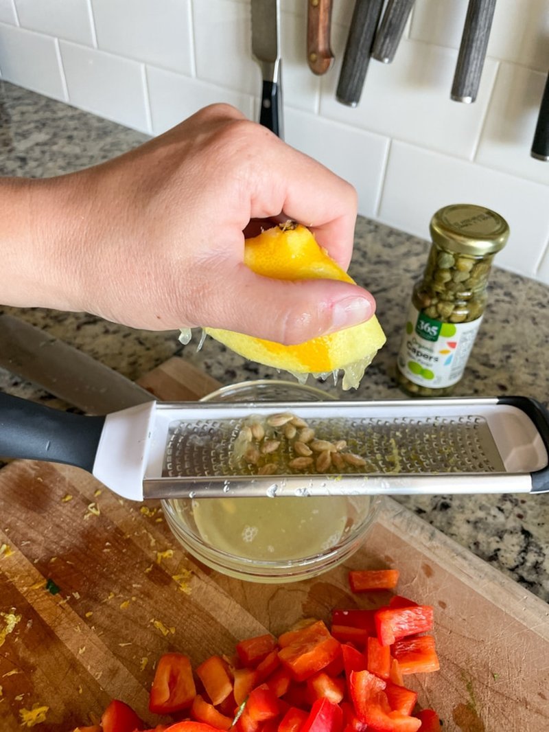 Squeezing lemon juice over a glass bowl of prepared ingredients