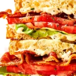 BLT sandwich stacked on white plate, rosemary mayo visible
