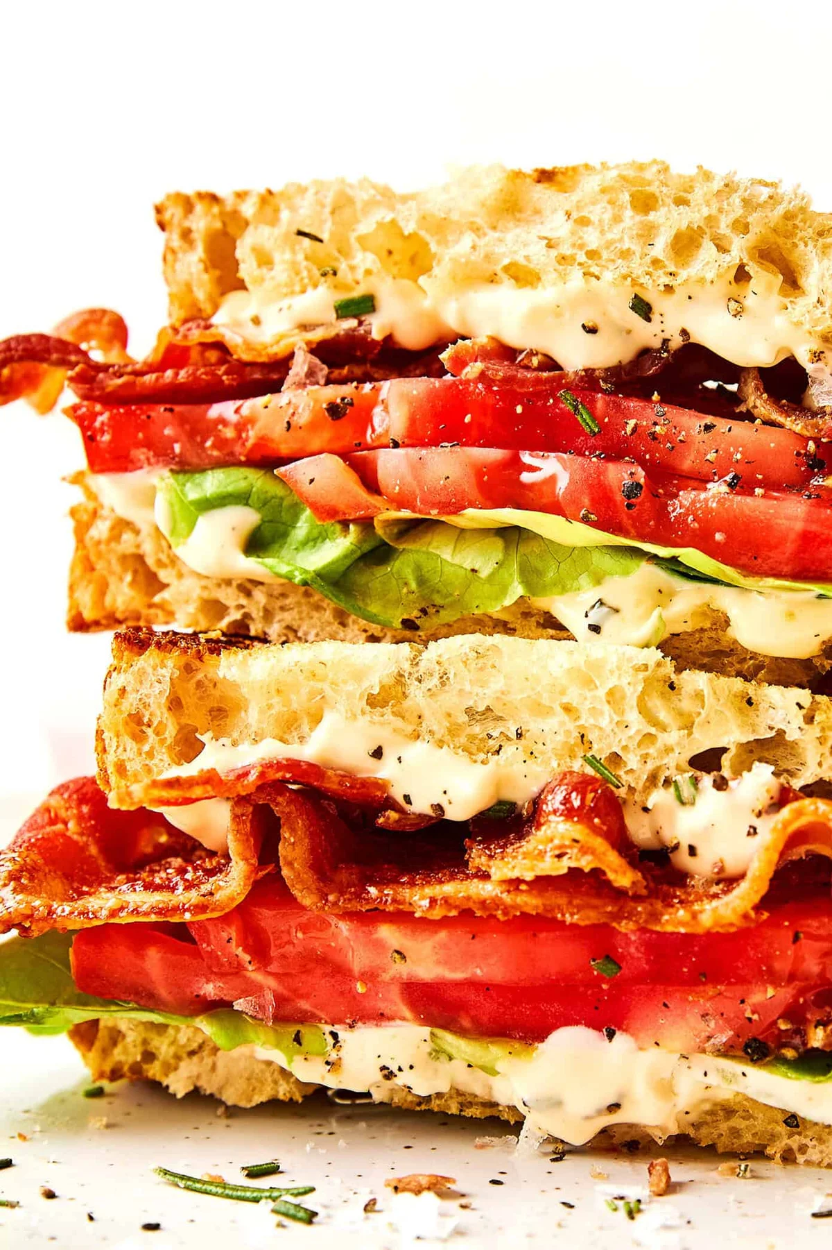 BLT sandwich stacked on white plate, rosemary mayo visible