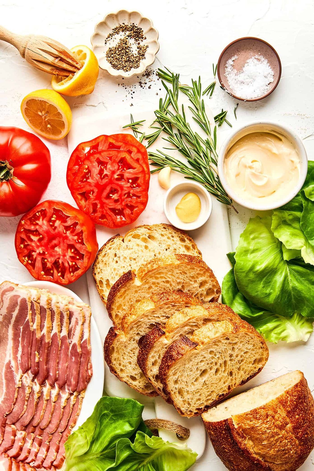 Fresh BLT ingredients arranged flat-lay: bread, tomato, rosemary, mayo