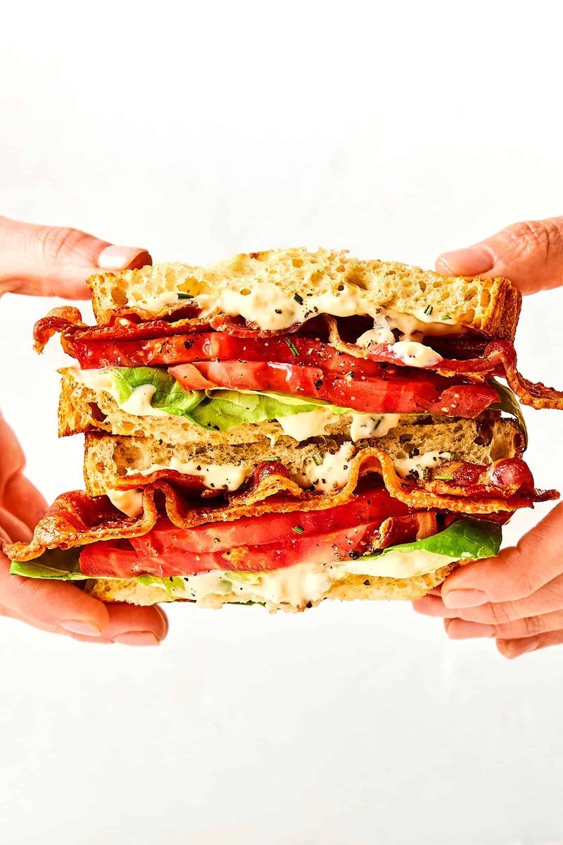 Hands holding a tall BLT sandwich with visible layers